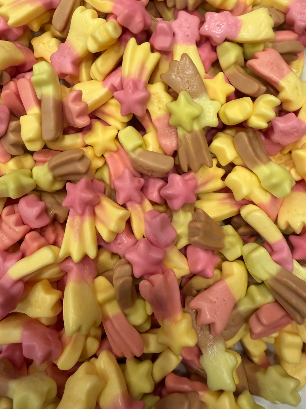 A close-up pile of small pastel candy pieces in pink, pale yellow, and light brown, including star and flower-shaped pieces.