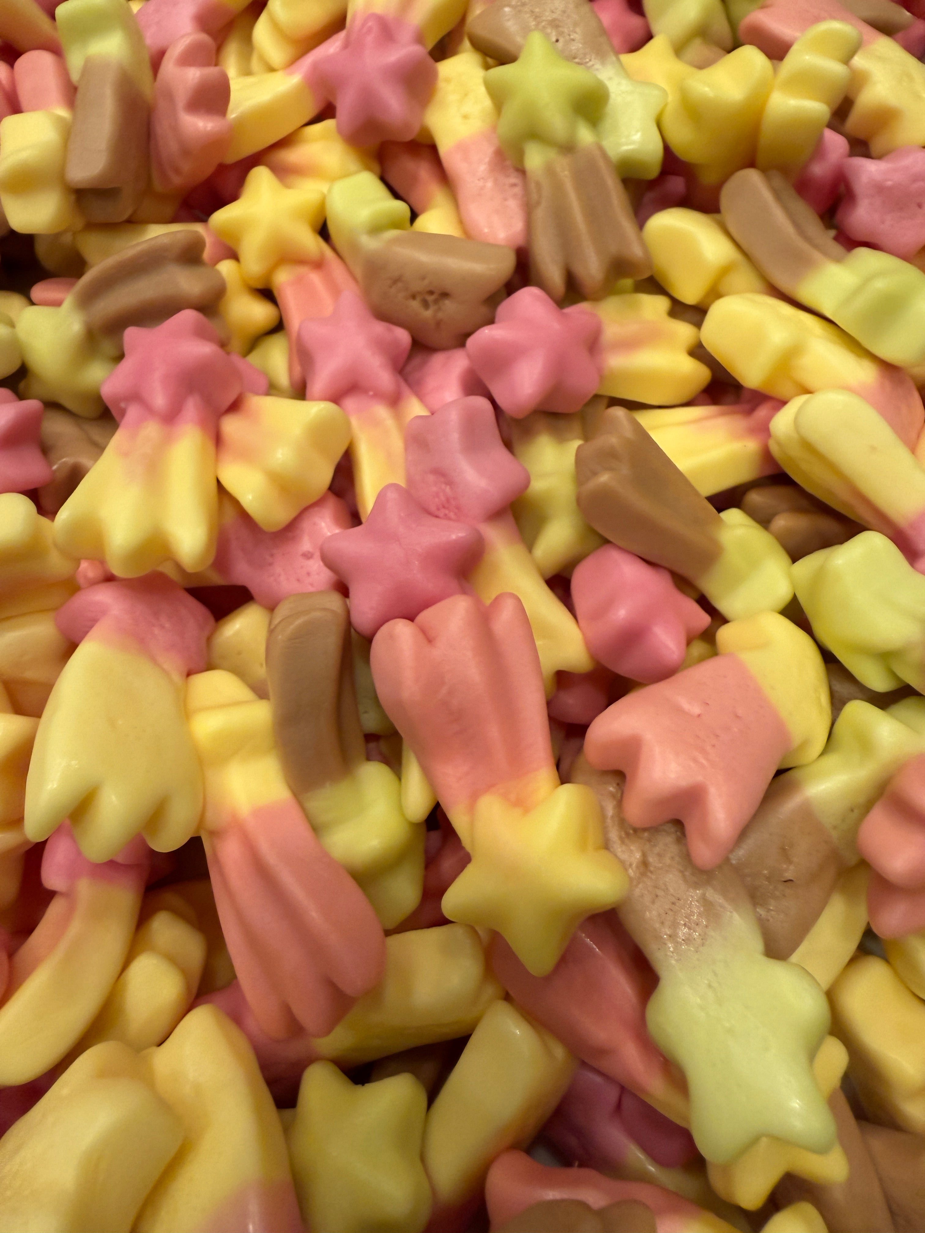 Overhead close-up of the shooting star gummy pile viewed at a slightly different angle, with pink, yellow, and tan star and flower shapes packed tightly together.