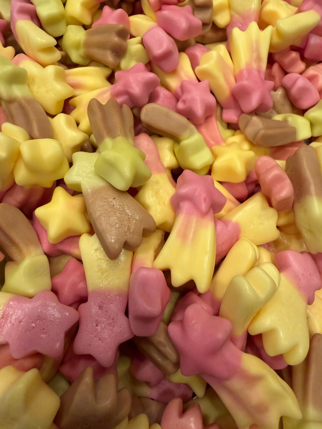 A close-up pile of small star-shaped candies in pastel pink, pale yellow, and light brown, filling the entire frame.