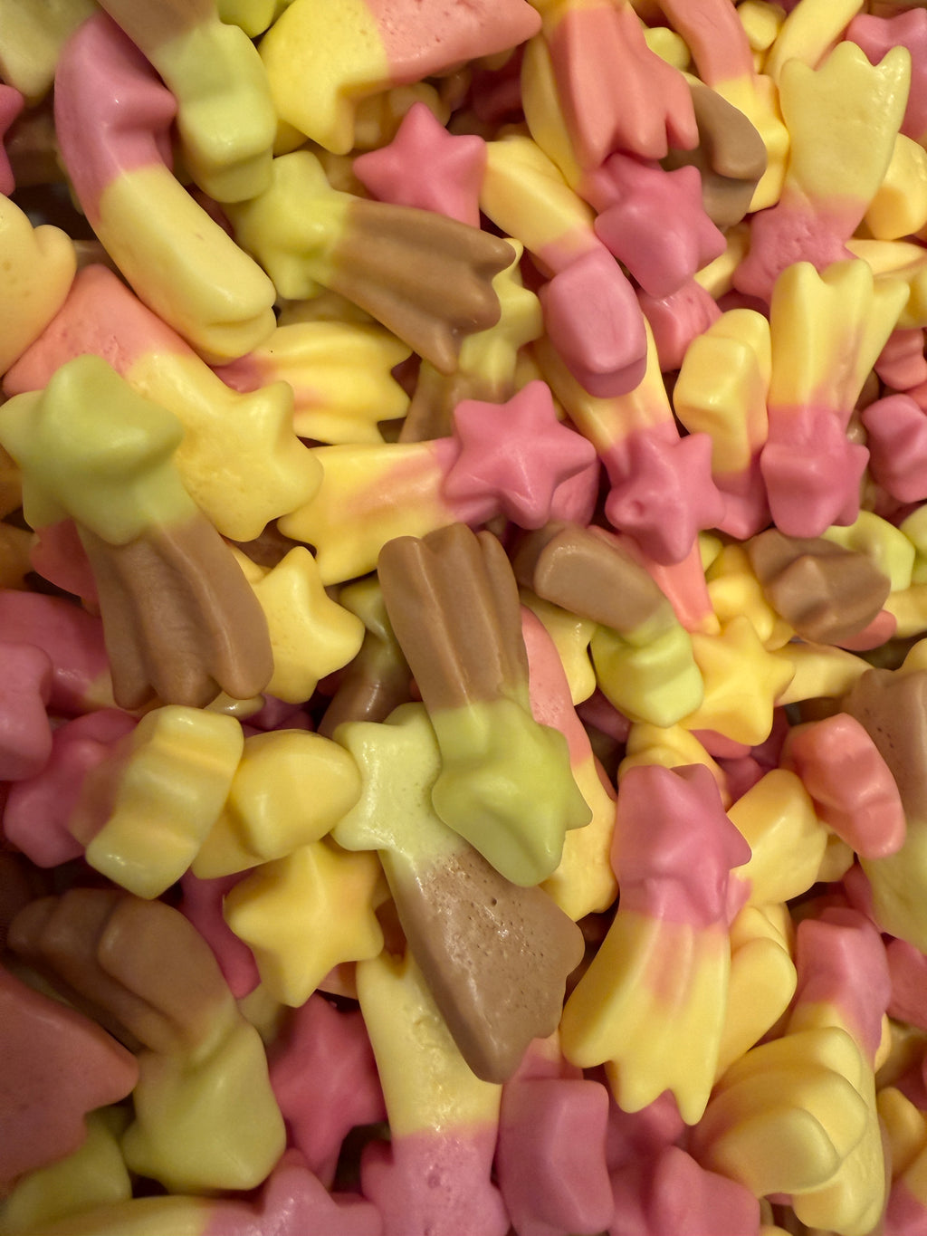 A close-up pile of pastel-colored star-shaped candies in pink, yellow, and brown.