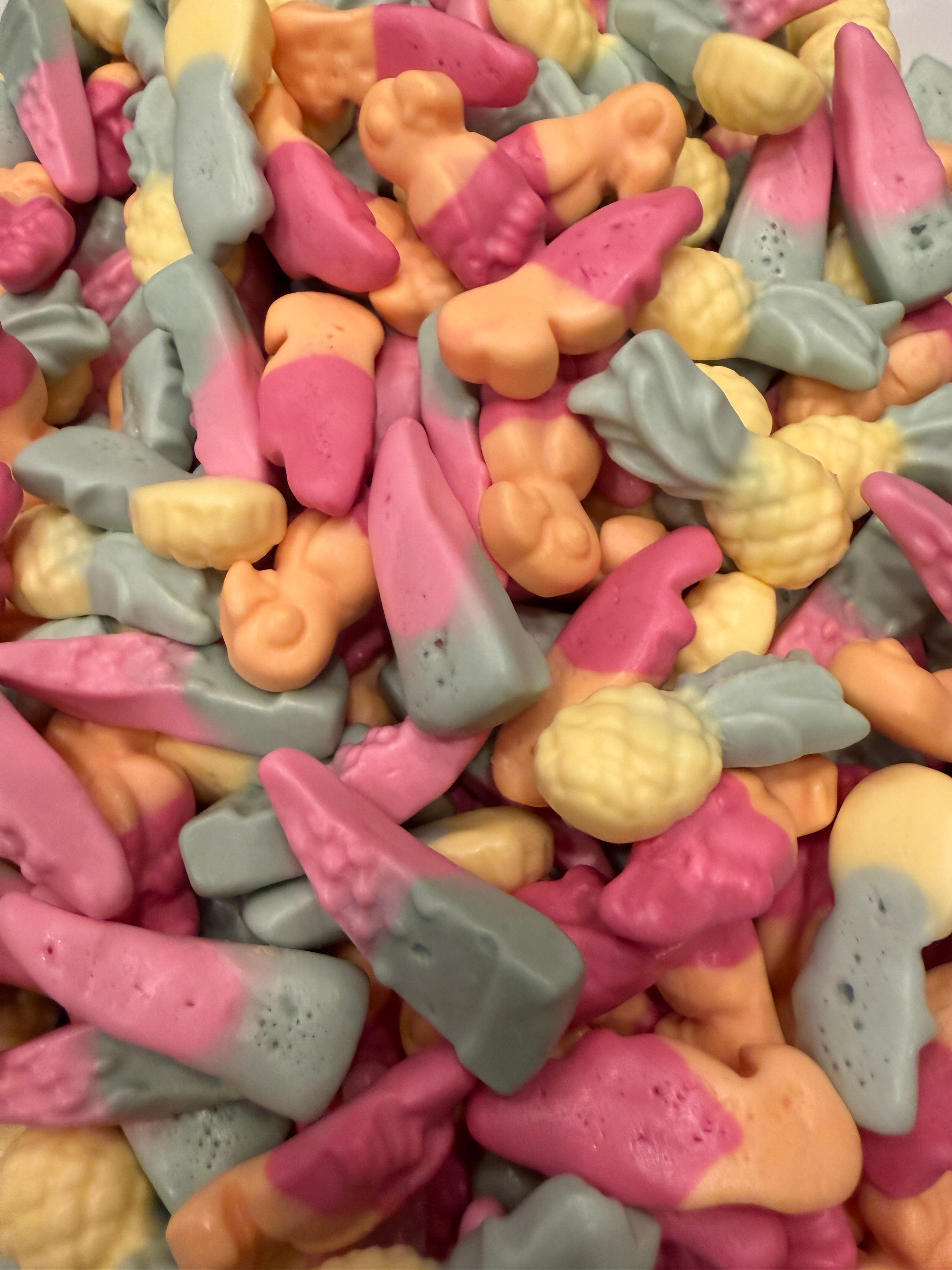 A close-up pile of small, colorful candy pieces in pink, pale yellow, and light gray, with some shaped like pineapples and others like small flowers or curls.