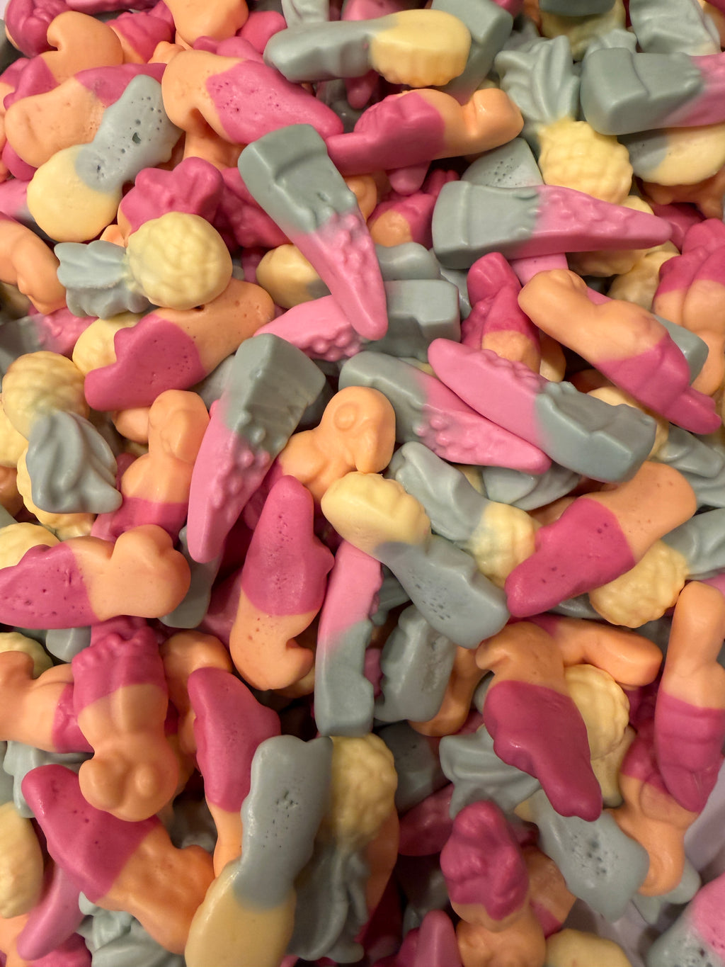 A close-up pile of small pastel candy pieces in pink, peach, pale yellow, and light gray, filling the entire frame.