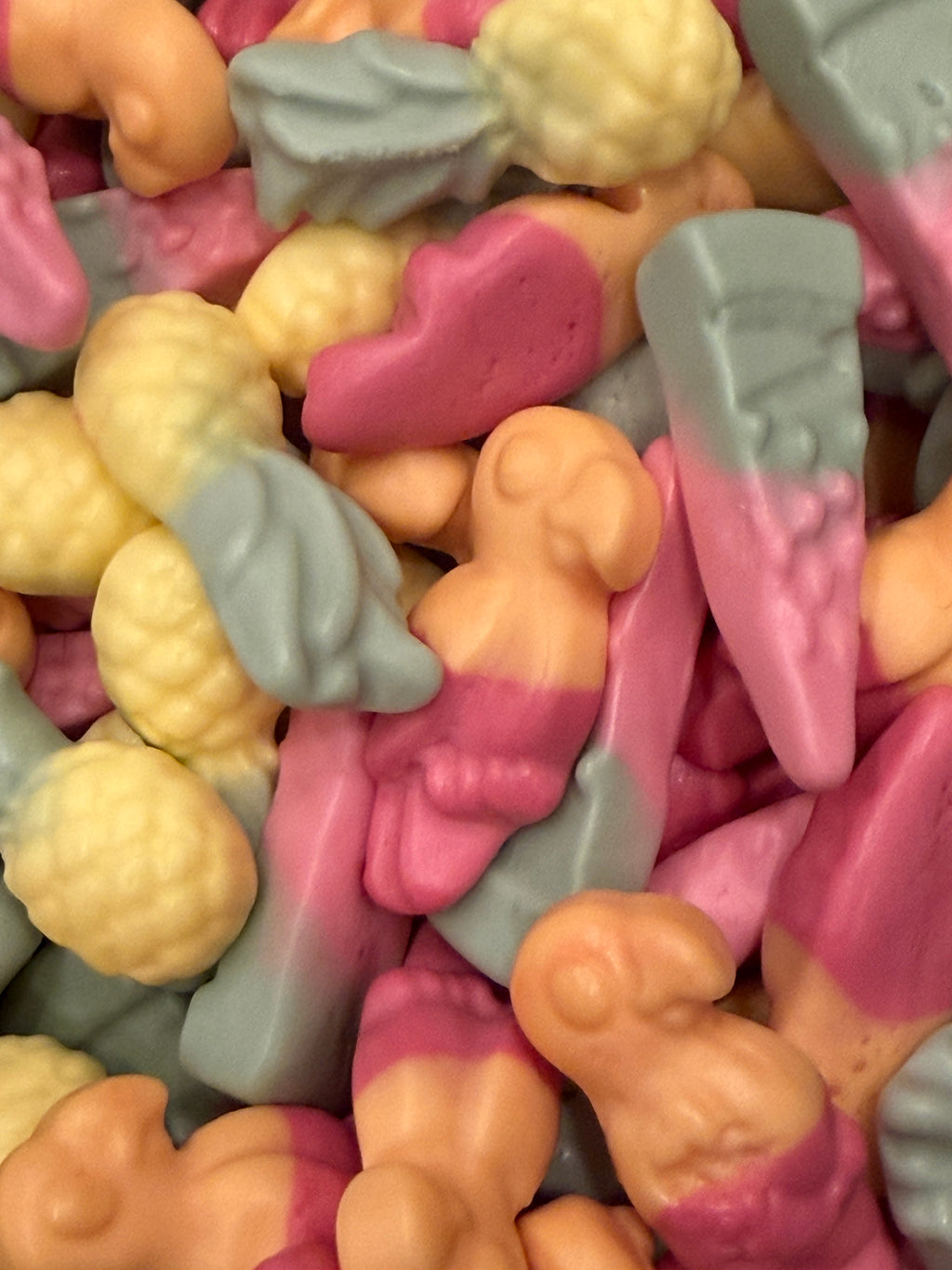 A close-up pile of small, novelty baby-shaped candies in pastel pink, peach, and light blue-gray colors.