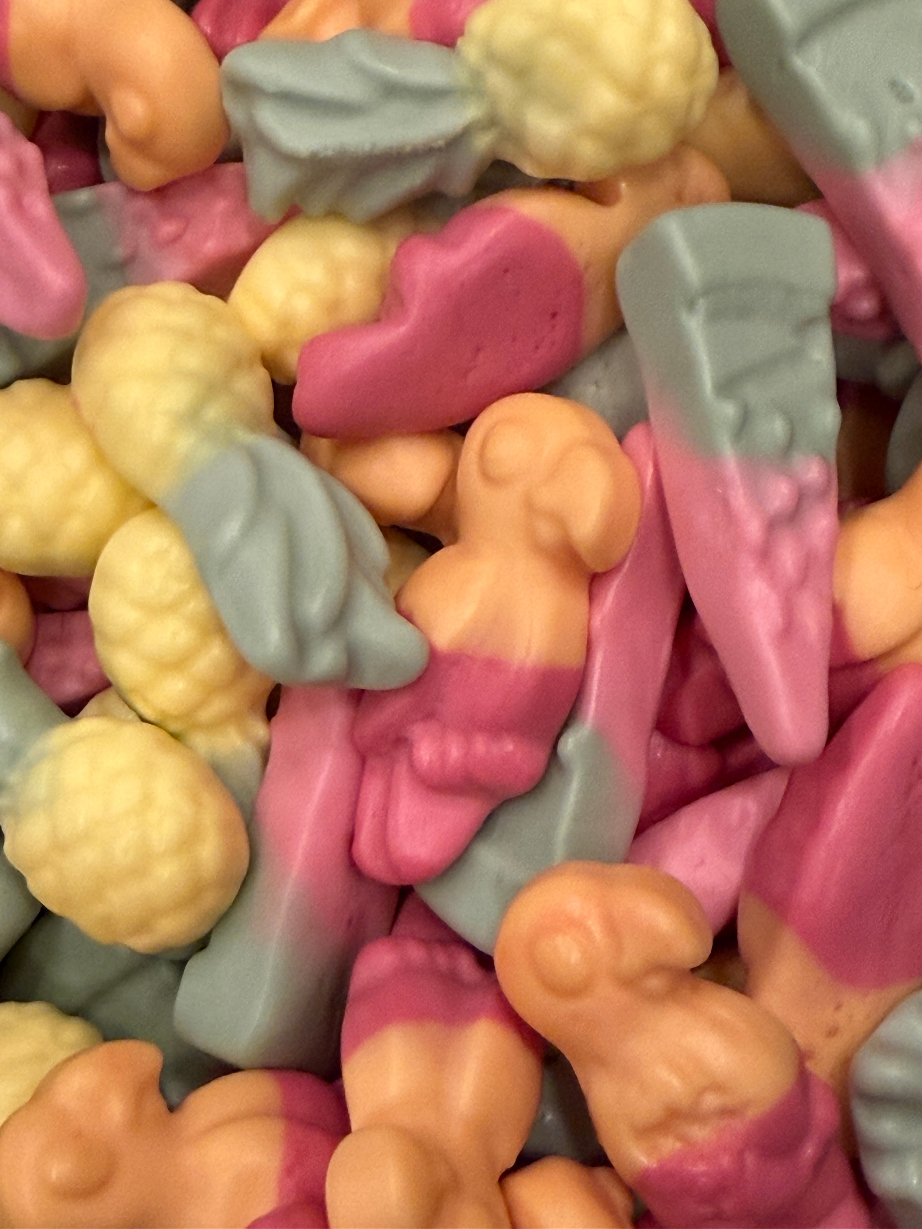 A close-up pile of small, novelty baby-shaped candies in pastel pink, peach, and light blue-gray colors.
