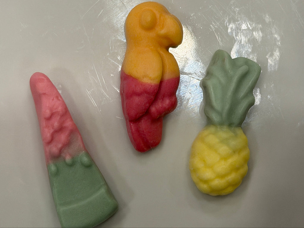 Three colorful gummy candies shaped like a watermelon slice, a parrot, and a pineapple