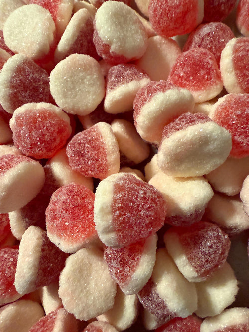 A close-up pile of sugar-dusted red and cream teardrop-shaped berry vanilla candies.