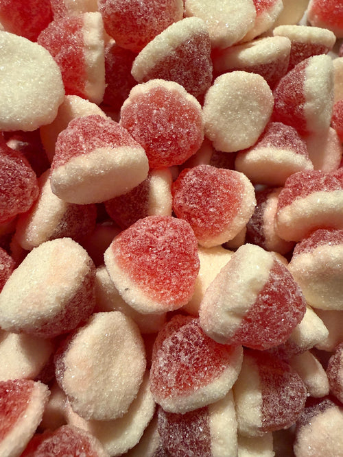 An overhead close-up of teardrop berry vanilla candies packed tightly together, with a few darker maroon-tinted pieces mixed among the bright red and cream ones.